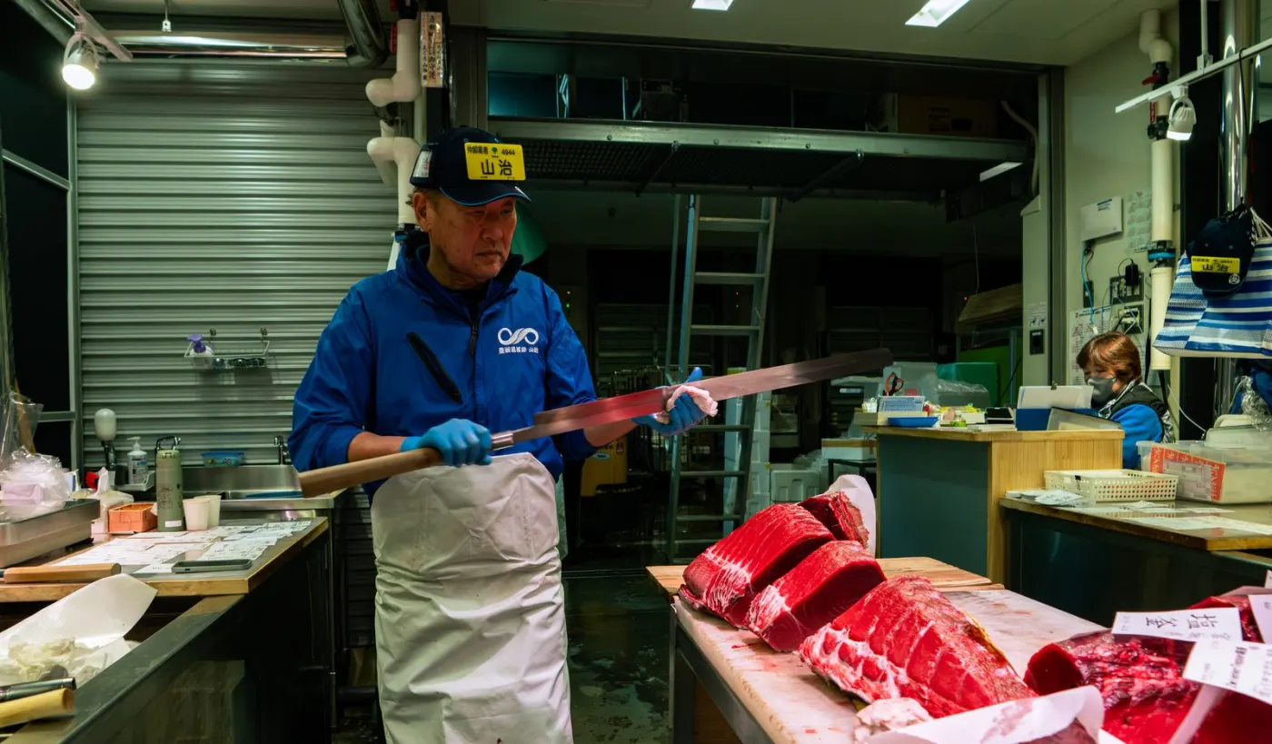 A Yamaharu tuna wholesaler with a long knife over bluefin loins